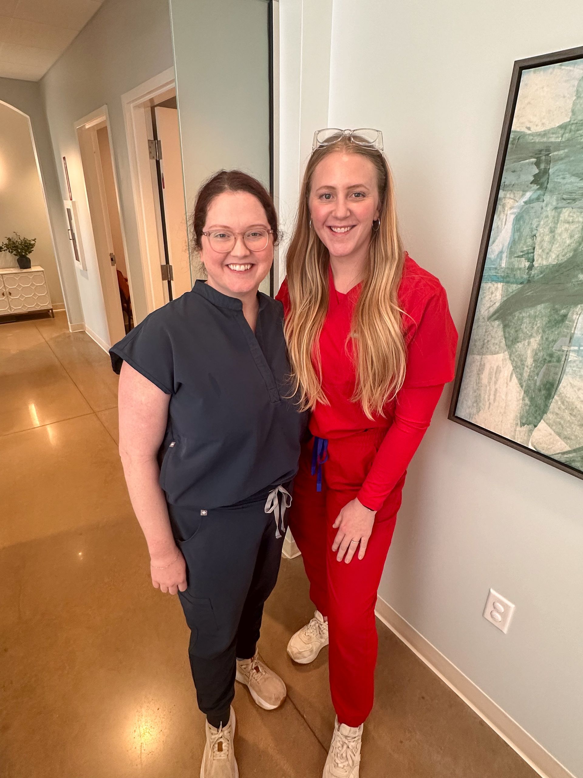 Two women in scrubs are standing next to each other in a hallway.