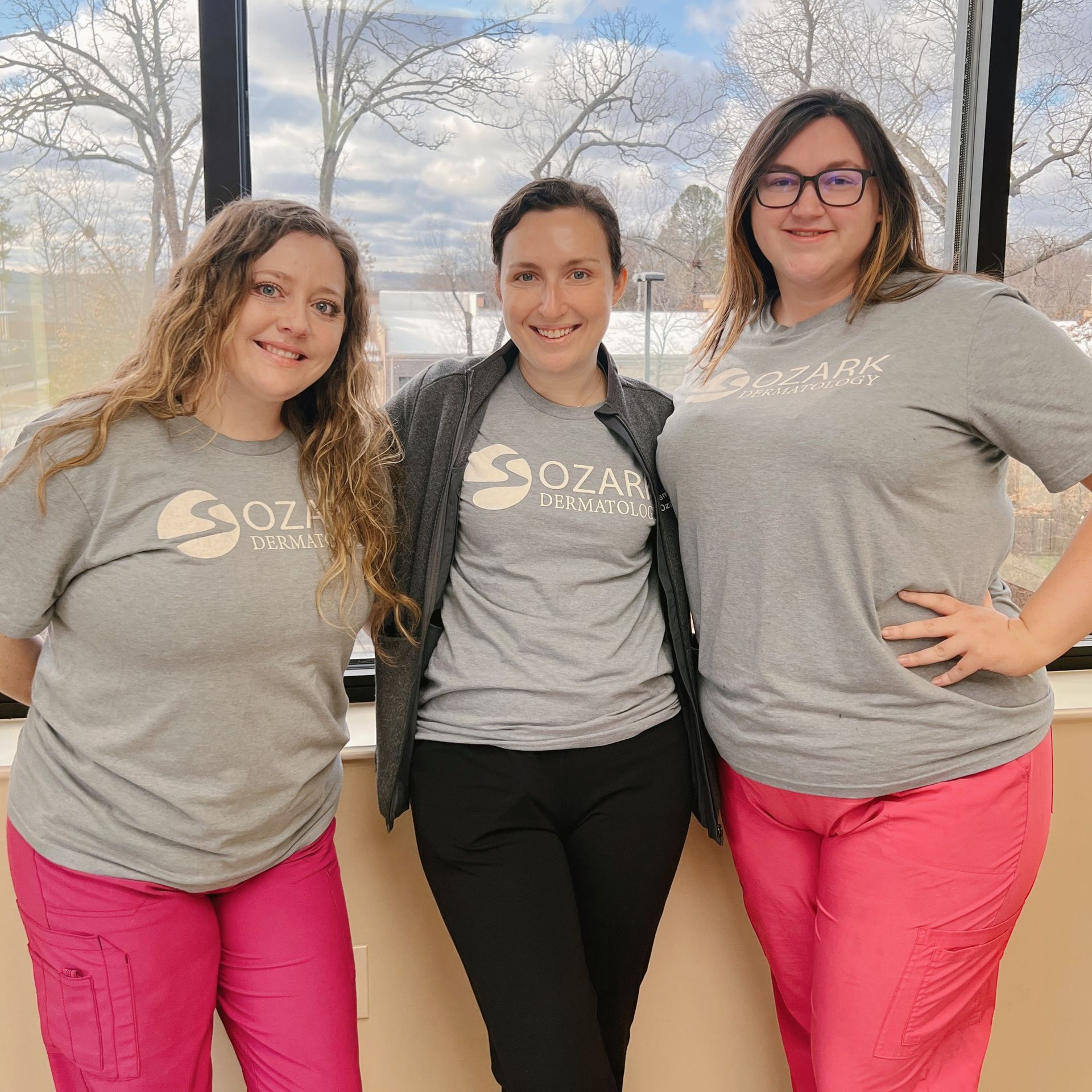 Three women are posing for a picture in front of a window.