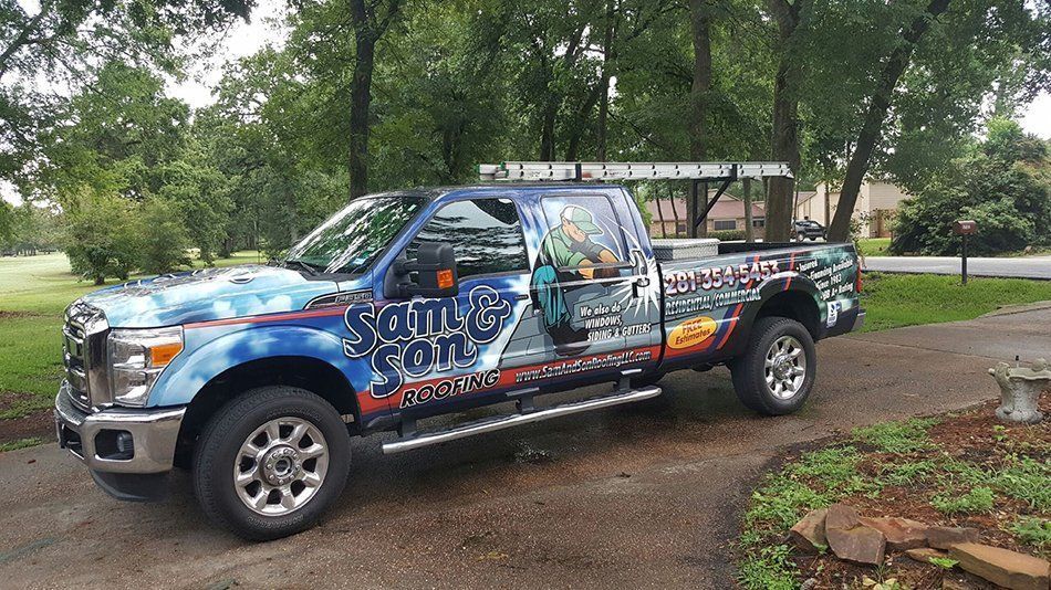 Blue pickup truck with company logo on the side, parked in a driveway. A ladder is mounted on the roof.