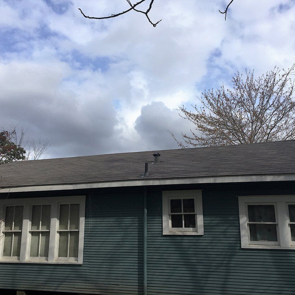 Blue house with white-framed windows against a cloudy sky. Bare tree branches in the background.