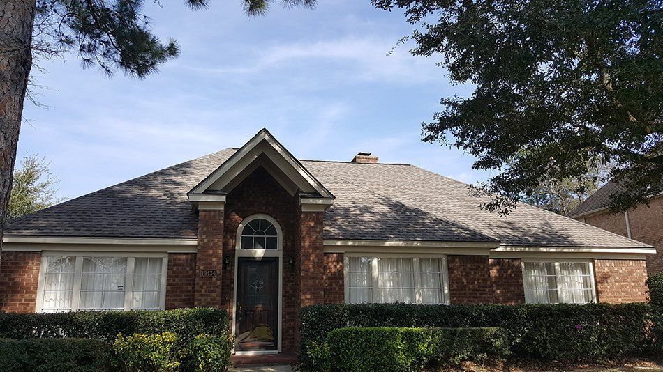 Brick house with arched doorway, symmetrical windows, and a brown roof under a blue sky.