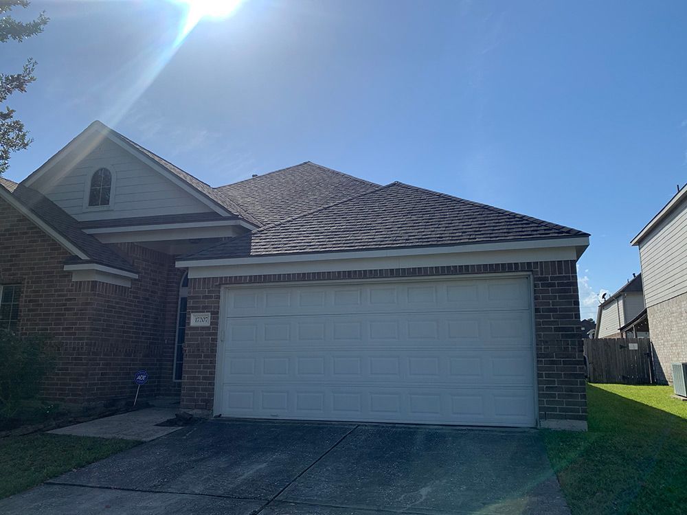 Brick house with white garage door and brown roof under a bright blue sky.