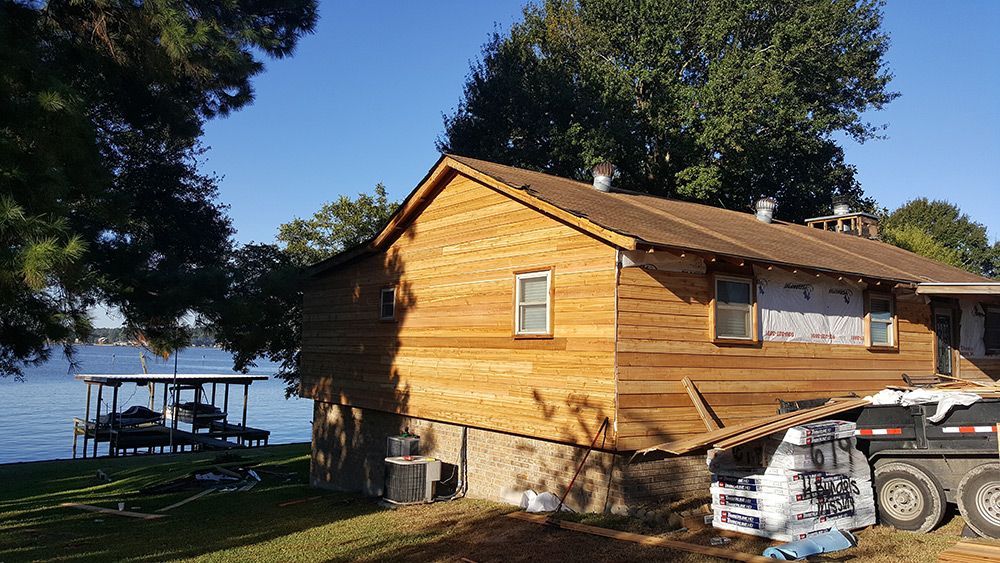 House with new wood siding under construction near a lake; boat dock in background.