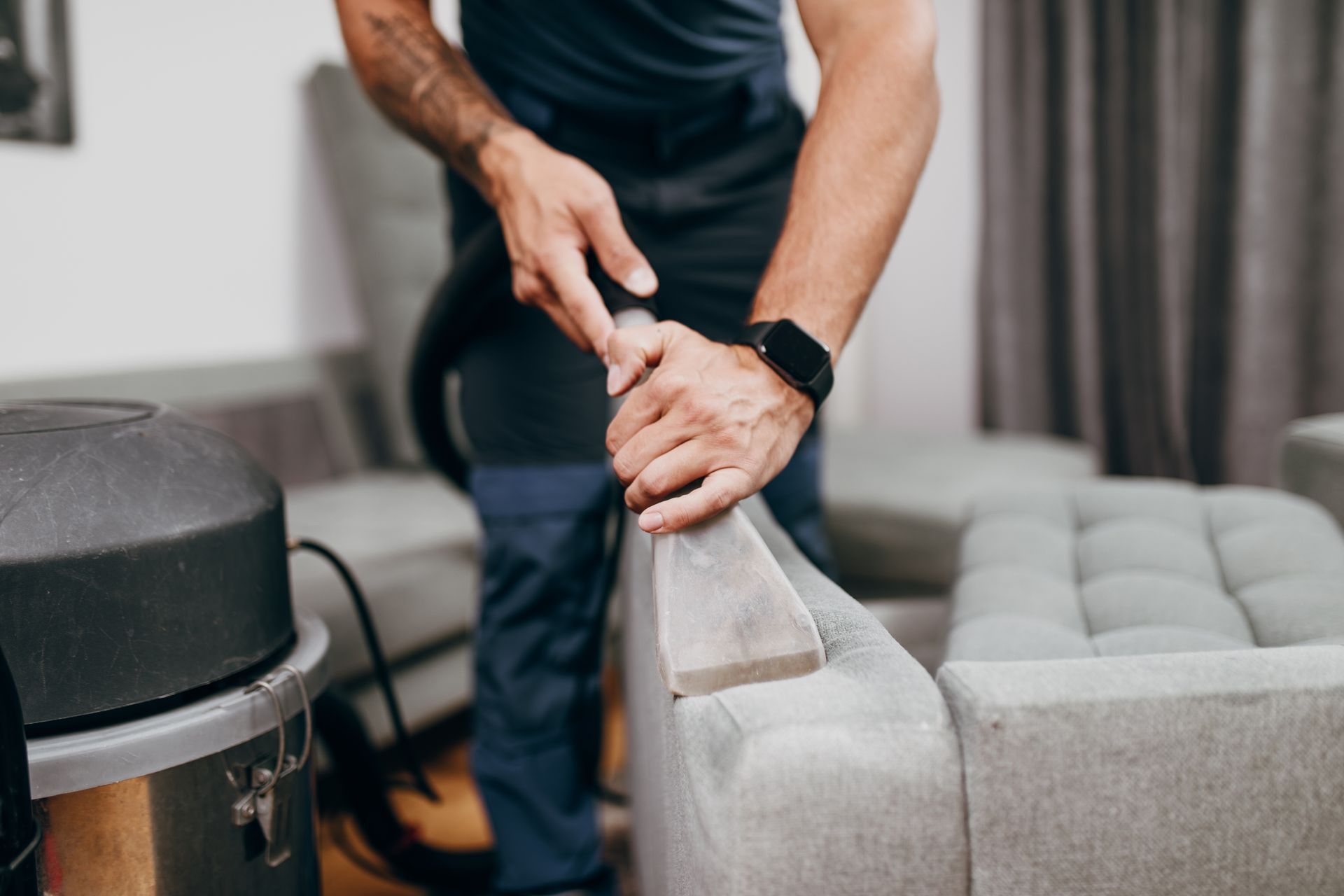 A man is cleaning a couch with a vacuum cleaner.