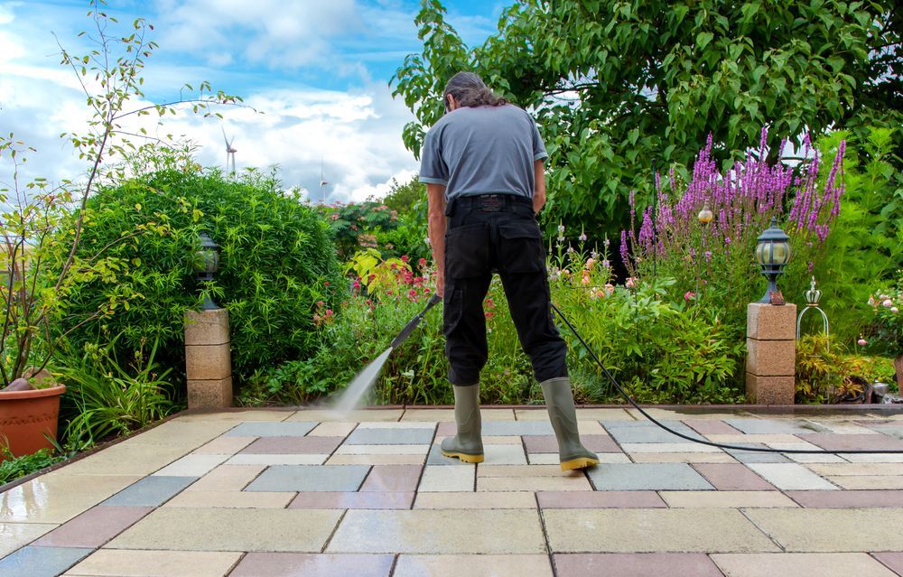 A man is cleaning a patio with a high pressure washer.