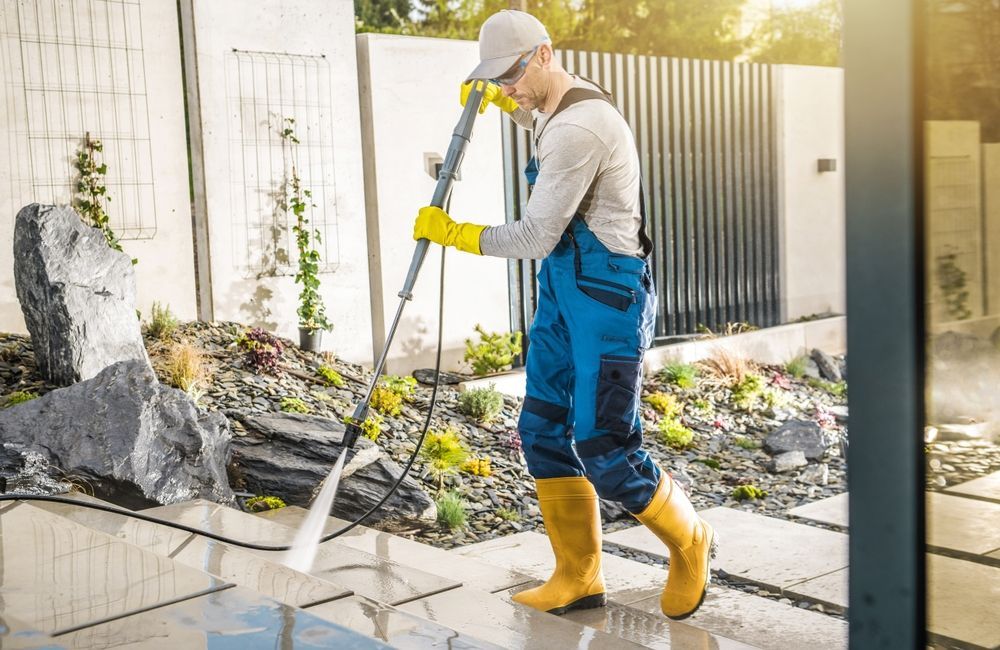 A man is using a high pressure washer to clean a patio.