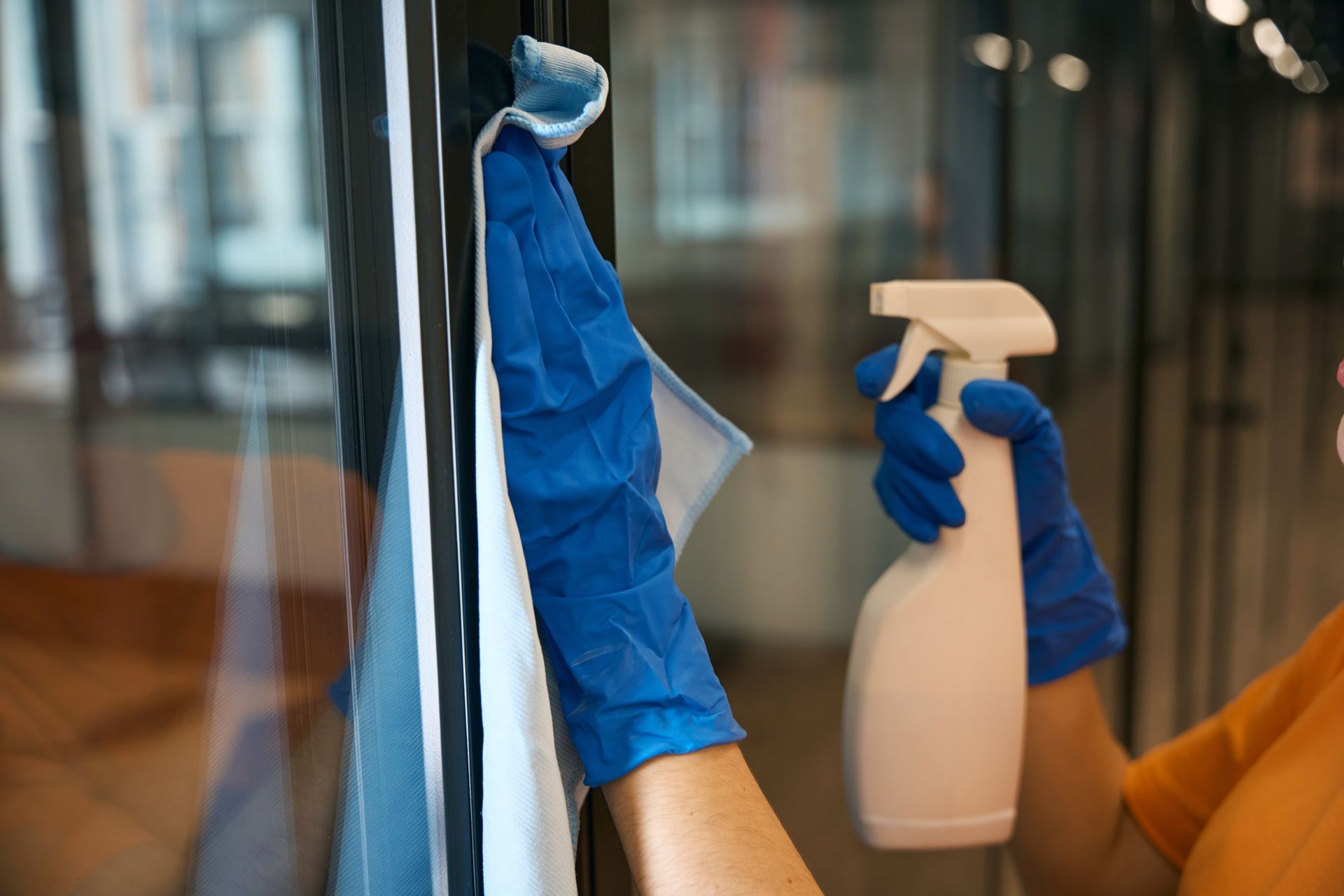 A woman is cleaning a glass door with a cloth and spray bottle.