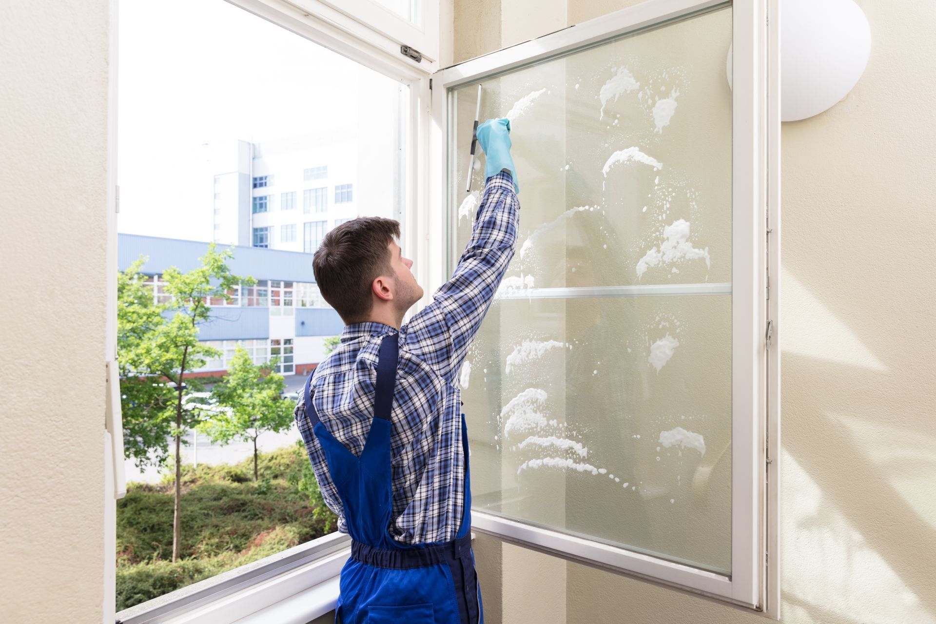 A person wearing yellow gloves is cleaning a window with a spray bottle and a cloth.