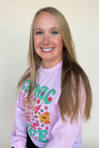 Woman in a pink sweater smiles, blonde hair, light background. Sweater says 