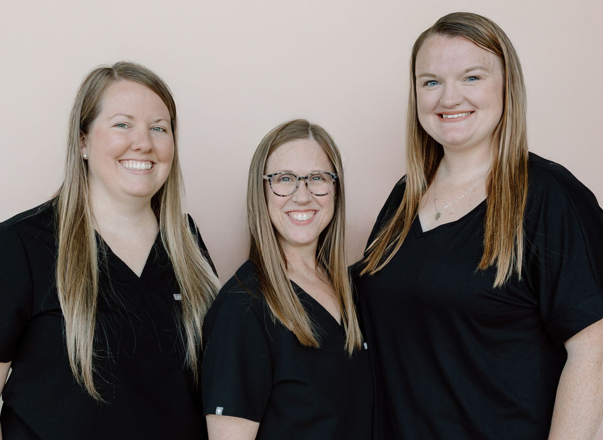 Three smiling people in black tops, standing in front of a pink wall.