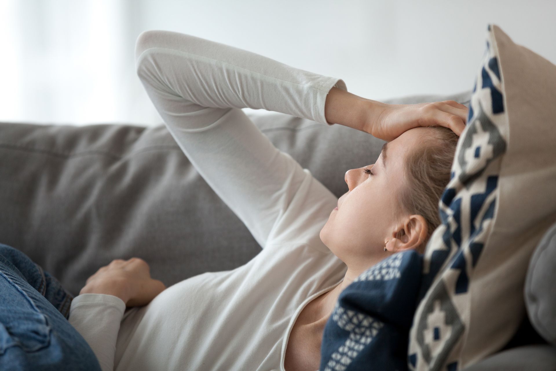 Woman lying on a couch, hand on her forehead, looking tired.