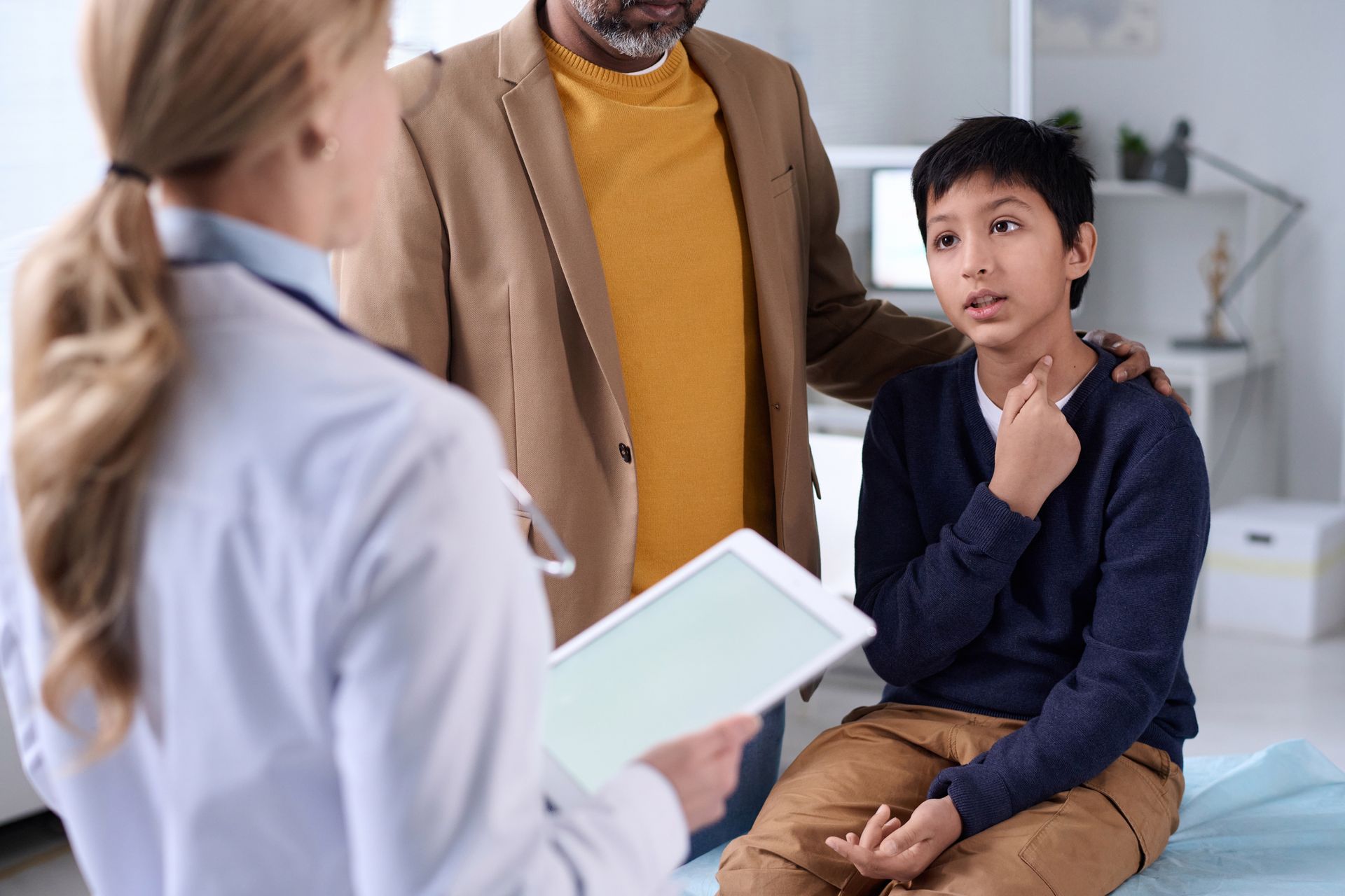 Doctor high-fives a child sitting with their parent in a medical office, all smiling.