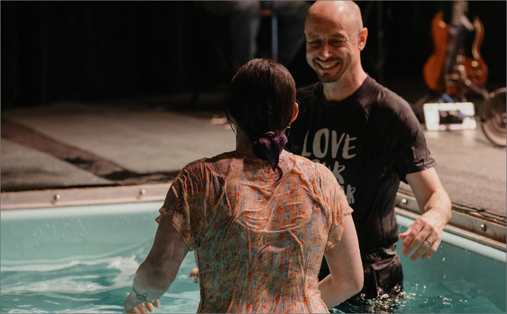 A man is baptising a woman in a swimming pool.