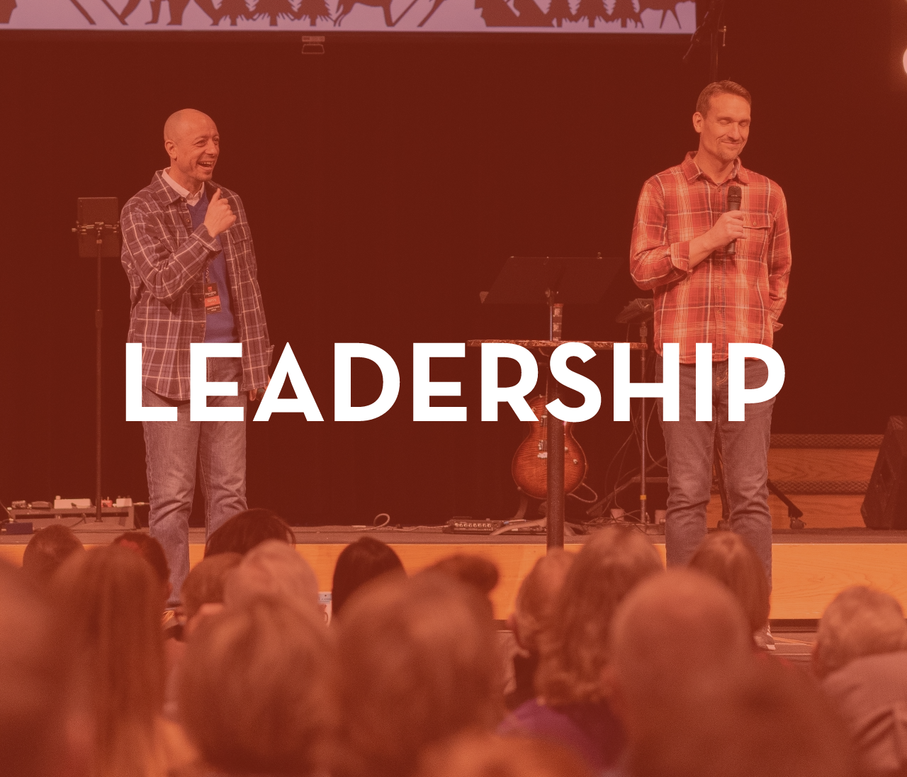 Two men are standing on a stage with microphones in front of a crowd.