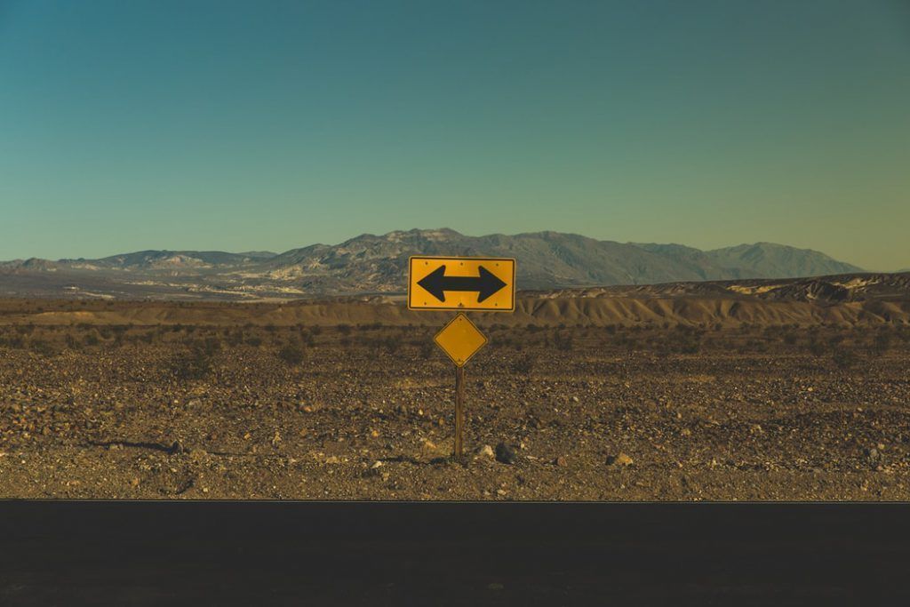A yellow sign with two arrows pointing in opposite directions in the middle of a desert.