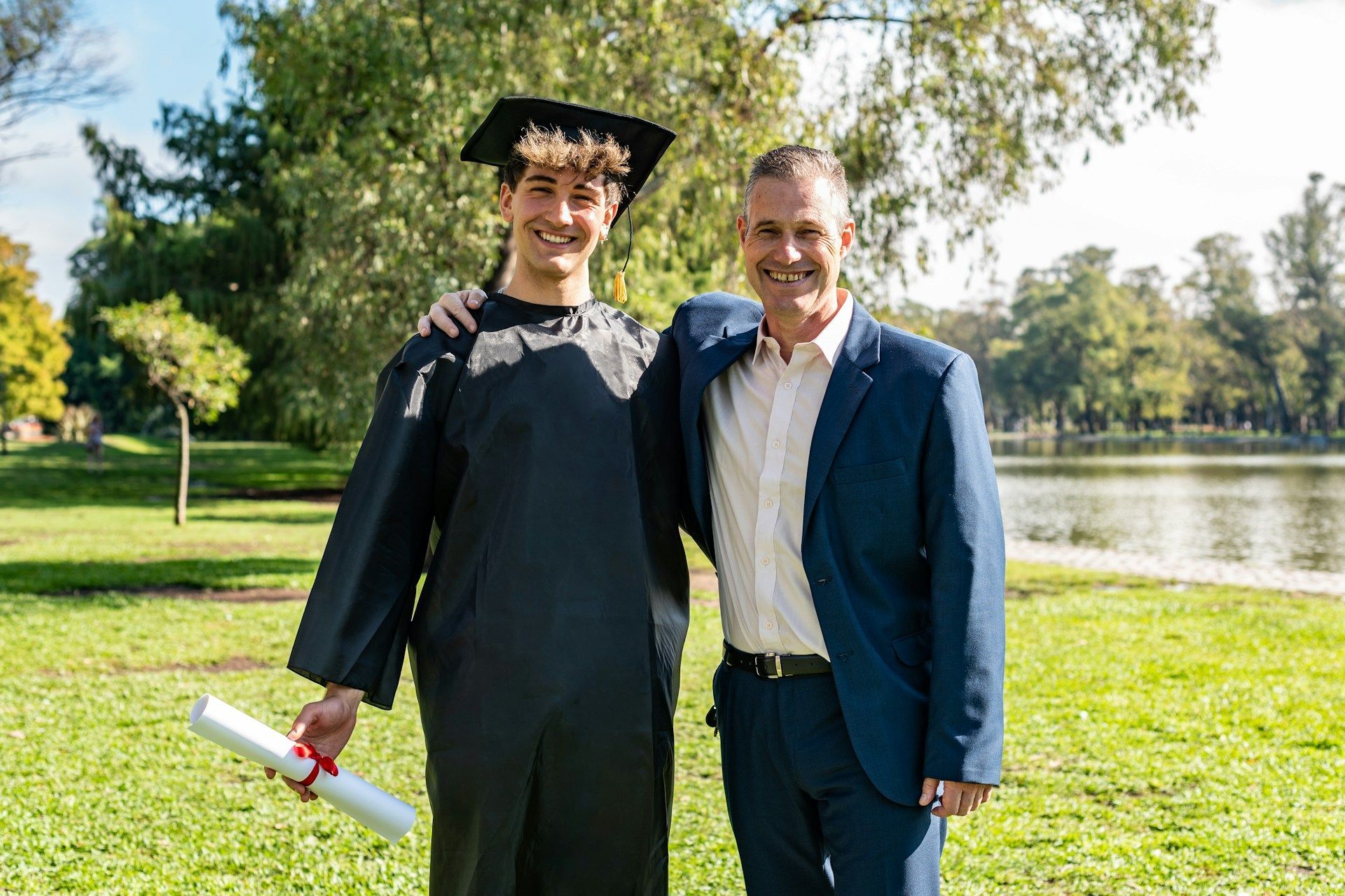 A man and a graduate are posing for a picture in a park.