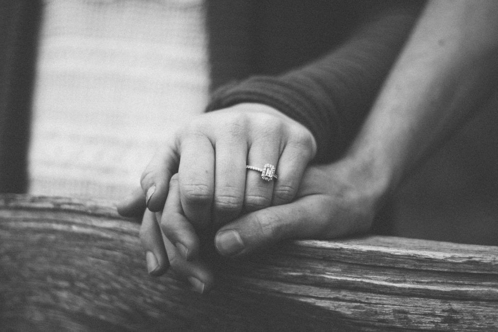 A black and white photo of a man and woman holding hands . the woman is wearing an engagement ring.