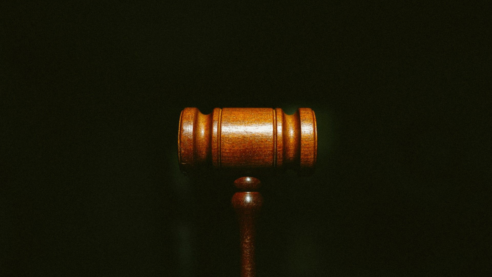 A wooden judge's gavel stands vertically against a solid black background.