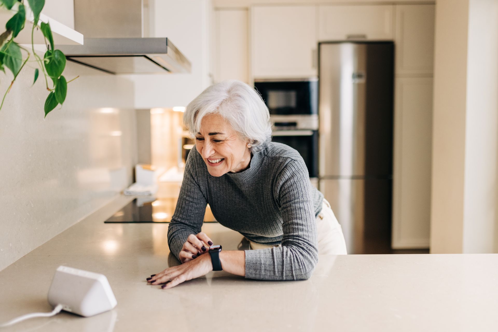 An older woman is laying on a kitchen counter looking at her smart watch.