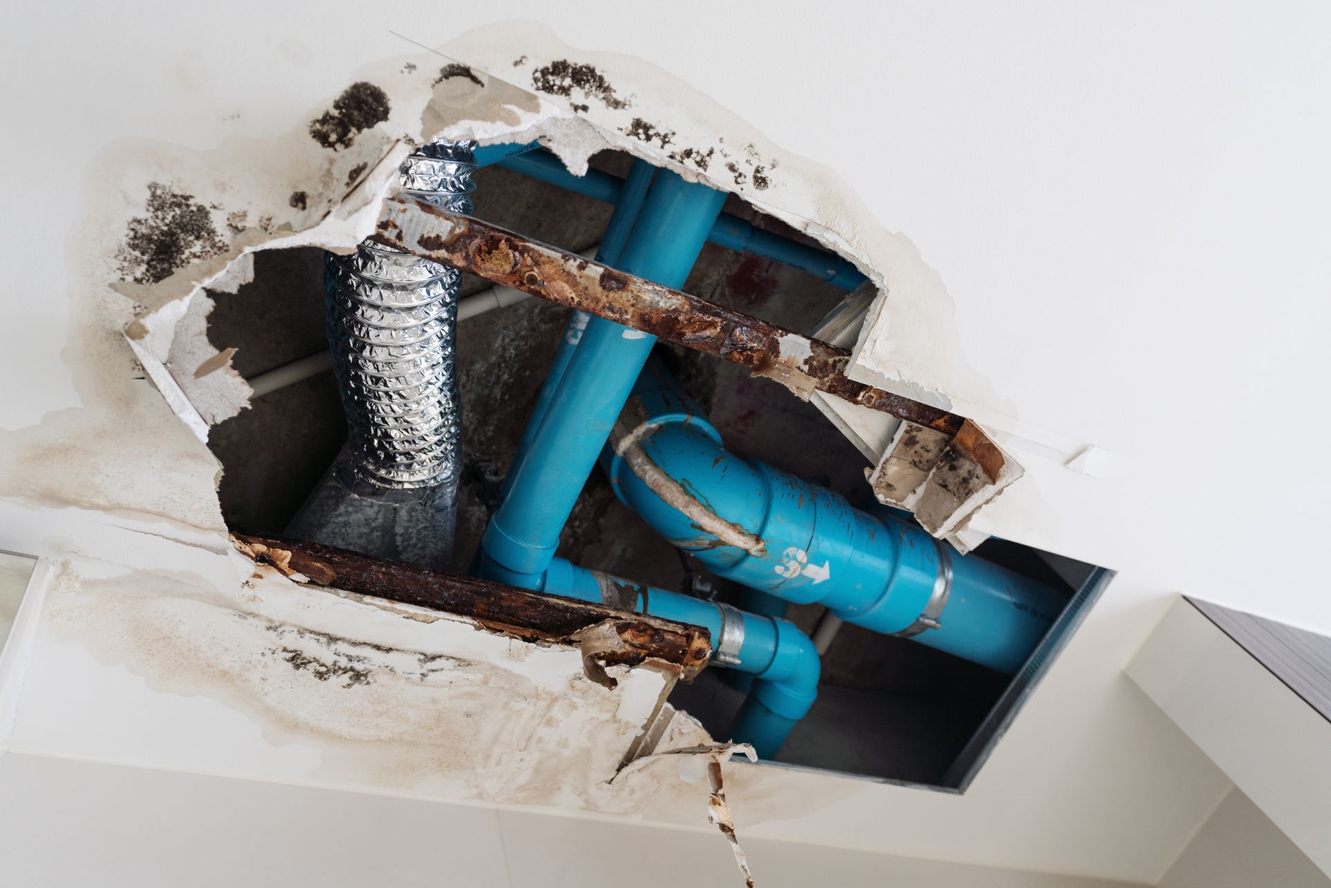 A hole in the ceiling with blue pipes coming out of it.