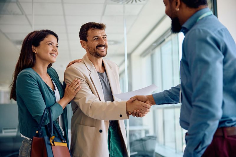 A man and woman are shaking hands with a man in an office.