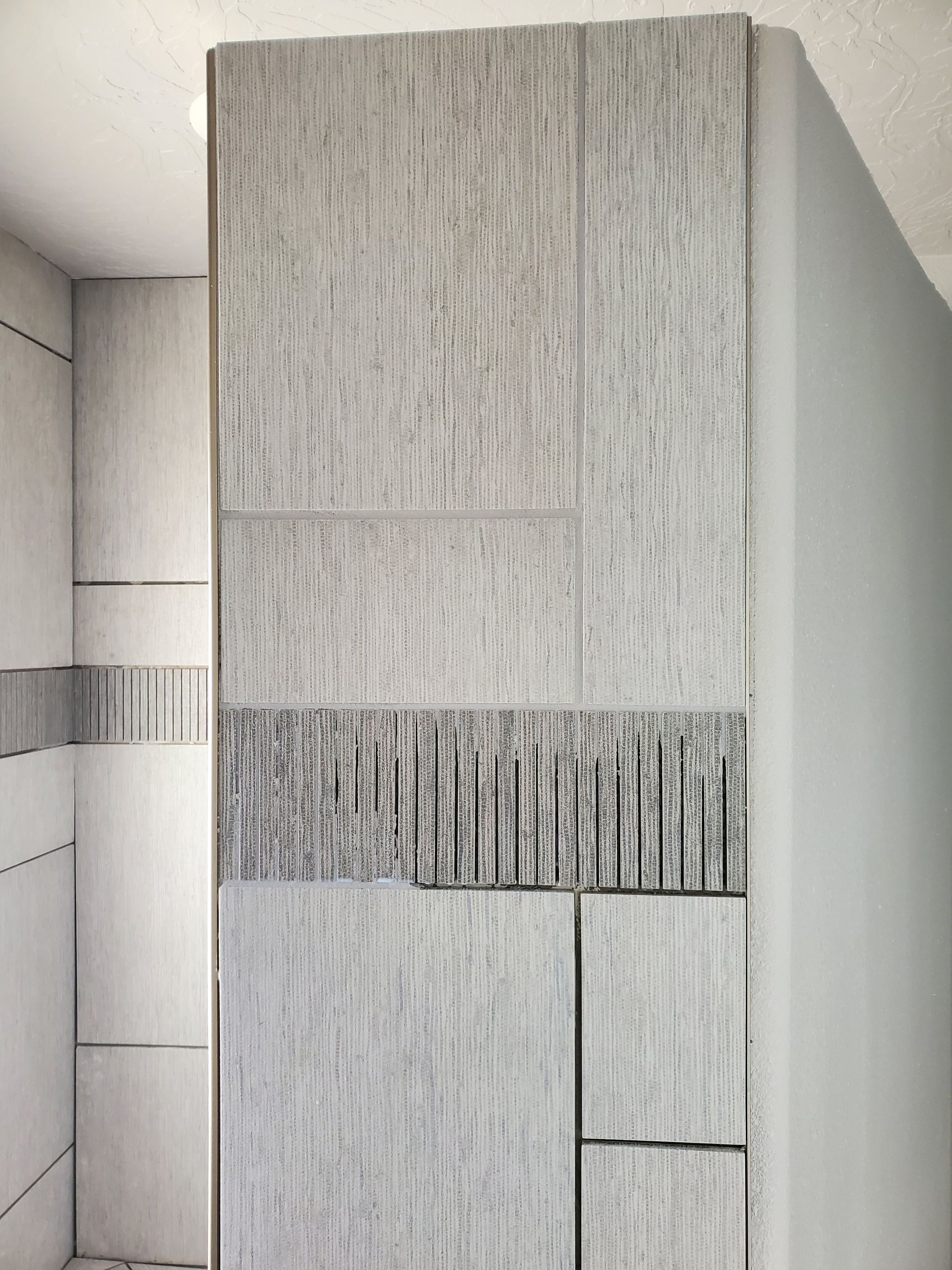 Gray textured wall tiles with horizontal and vertical designs in a bathroom setting.