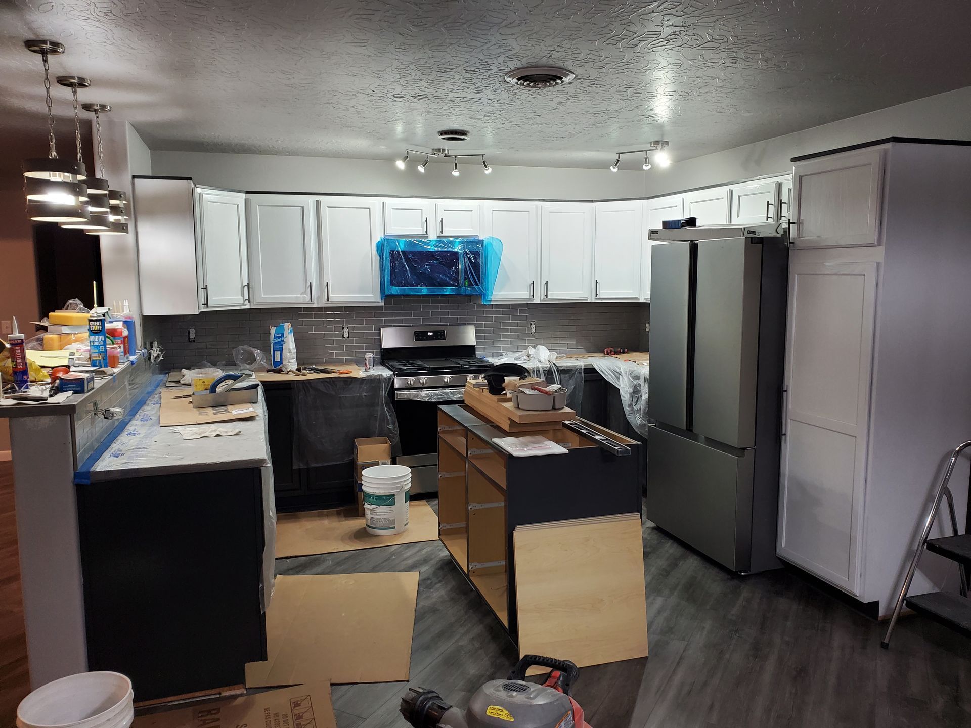 Kitchen undergoing renovation with gray cabinets, silver appliances, and light-colored walls.