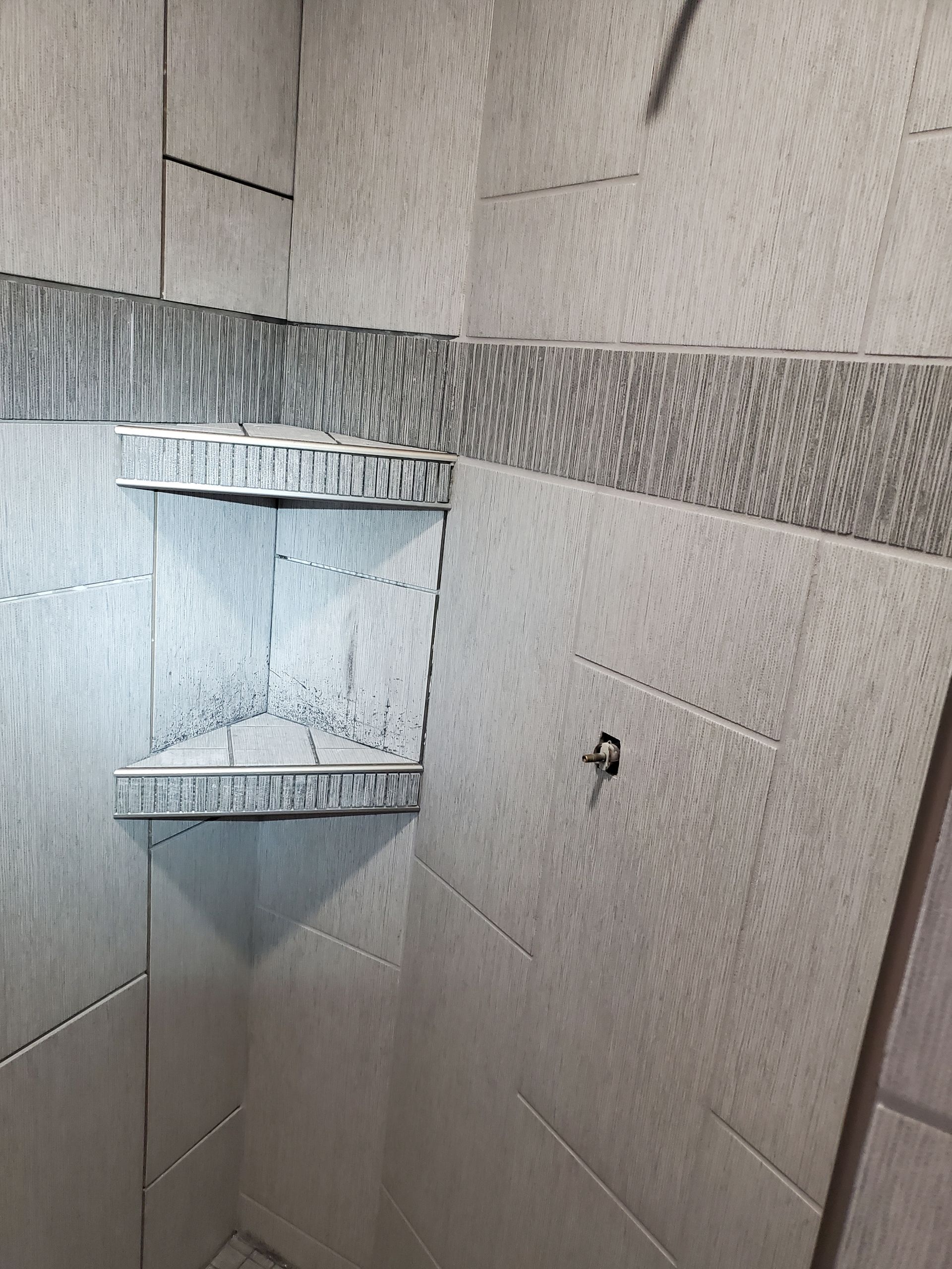 Gray tiled shower with corner shelves, recessed into the wall. Decorative tile border.