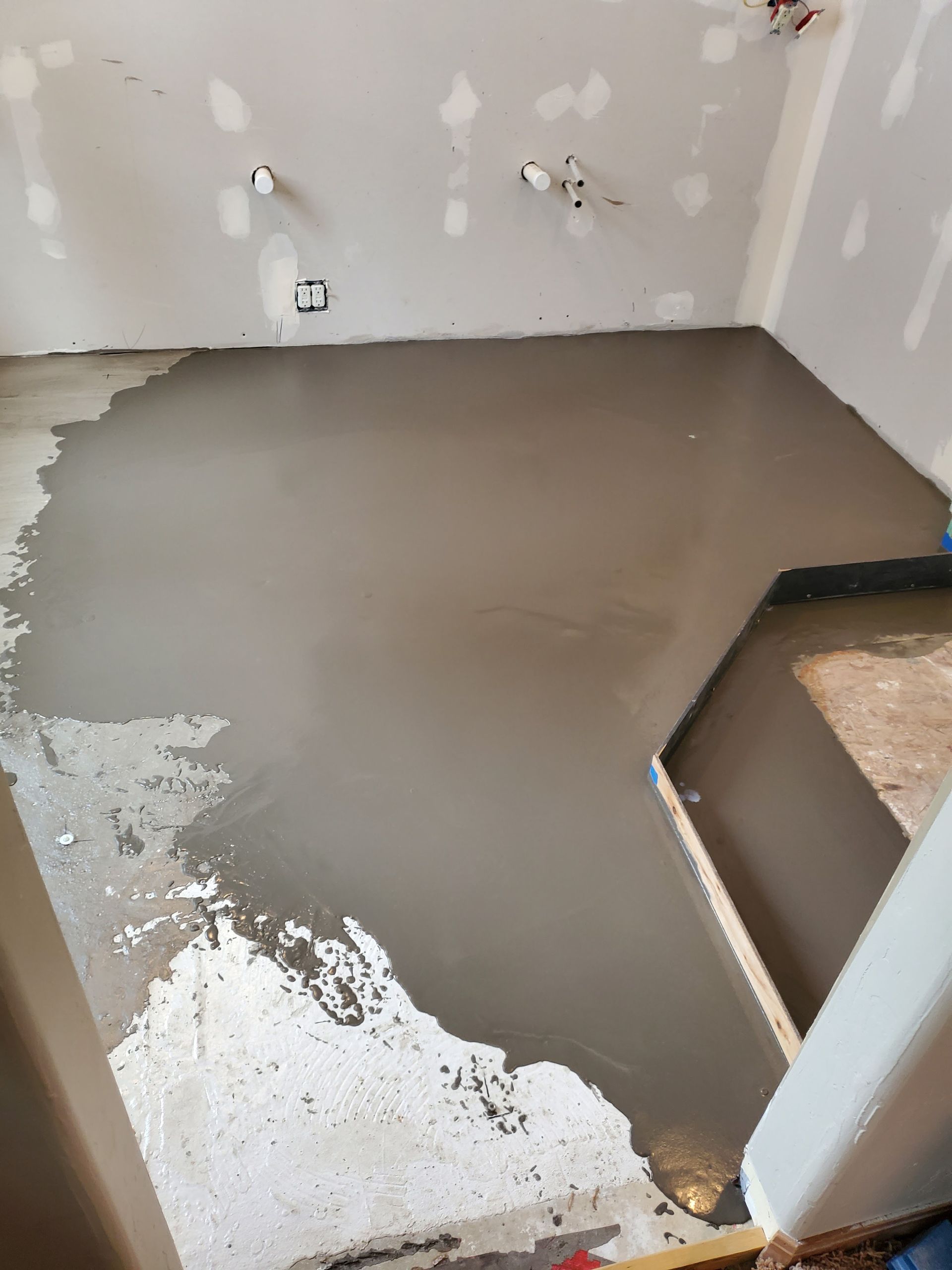 A room with a newly poured, wet concrete floor. Unfinished walls surround the floor.