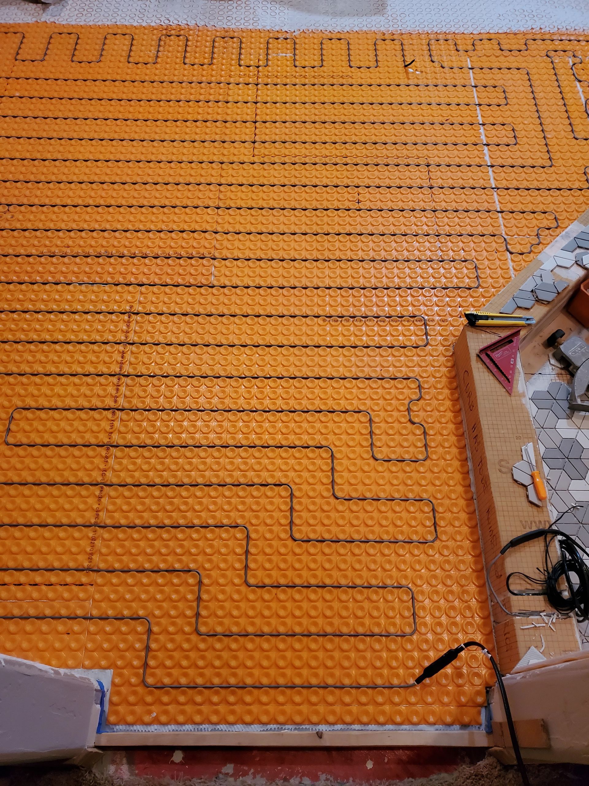 Orange heated floor mat with black heating cables laid out on a subfloor, ready for tiling.