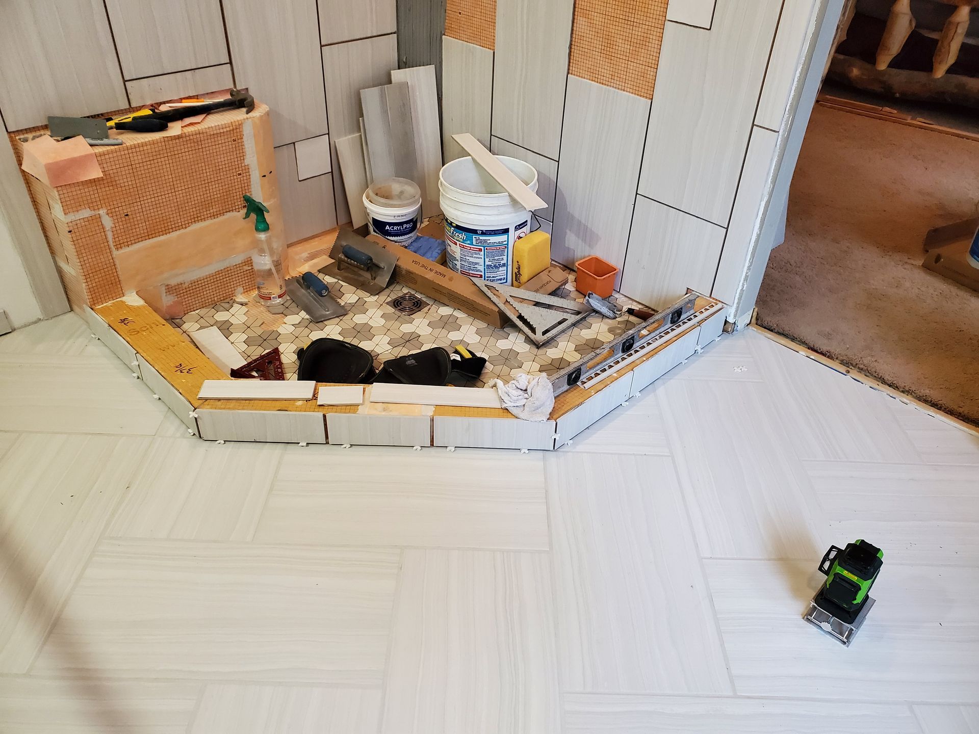 Construction site with tiled walls and floor. Tools and materials on a partially tiled alcove.