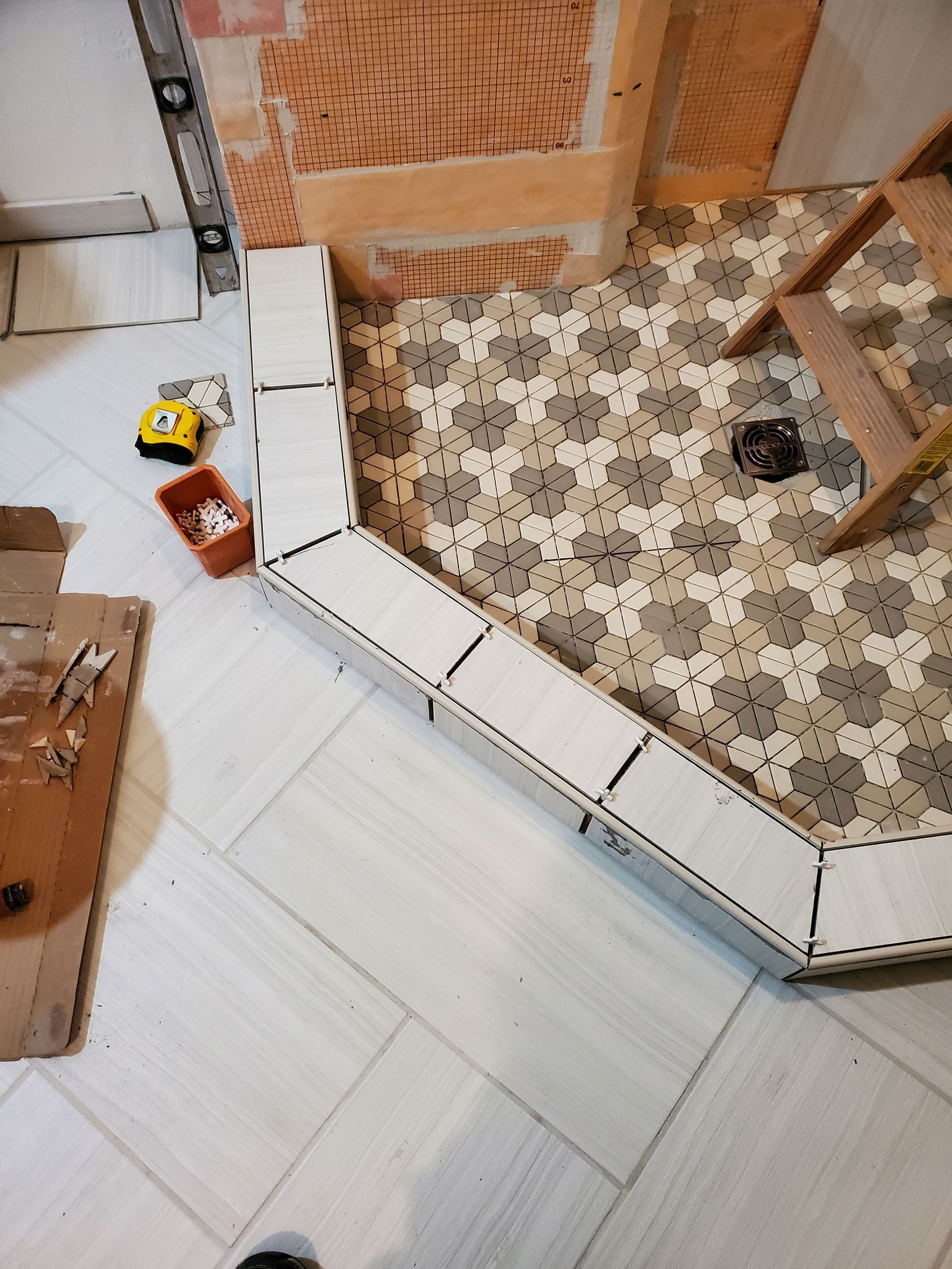Shower tile installation in progress; patterned floor tiles, white border, orange and beige accent tiles.