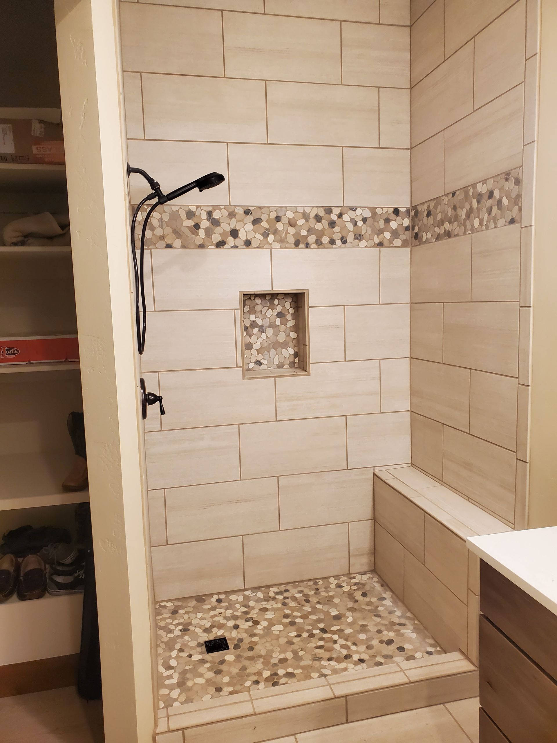 Tiled shower stall with a built-in bench and a pebble-stone floor; beige and brown tones.