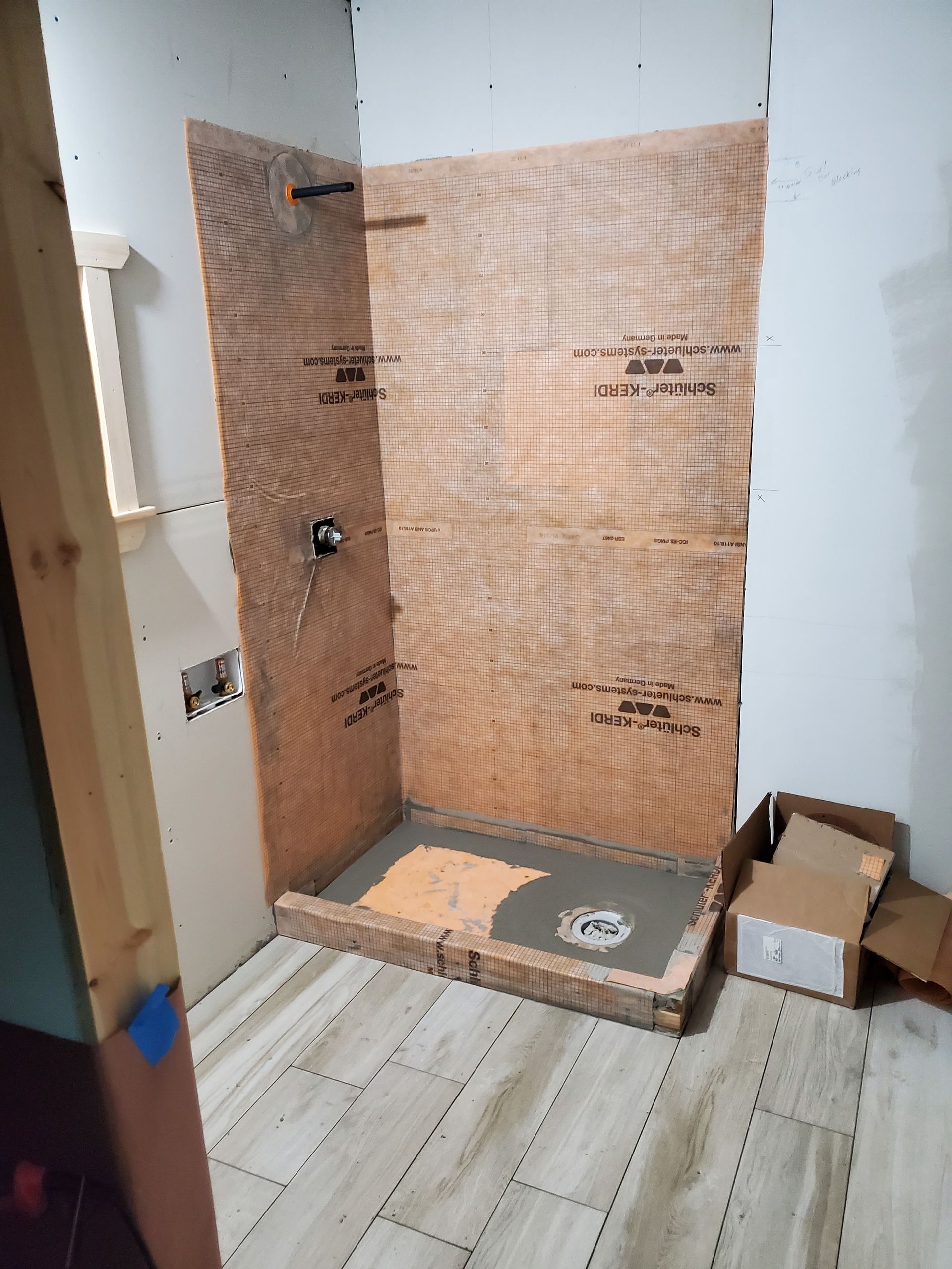 Shower stall under construction, featuring wood-like wall panels and a pre-sloped shower pan.