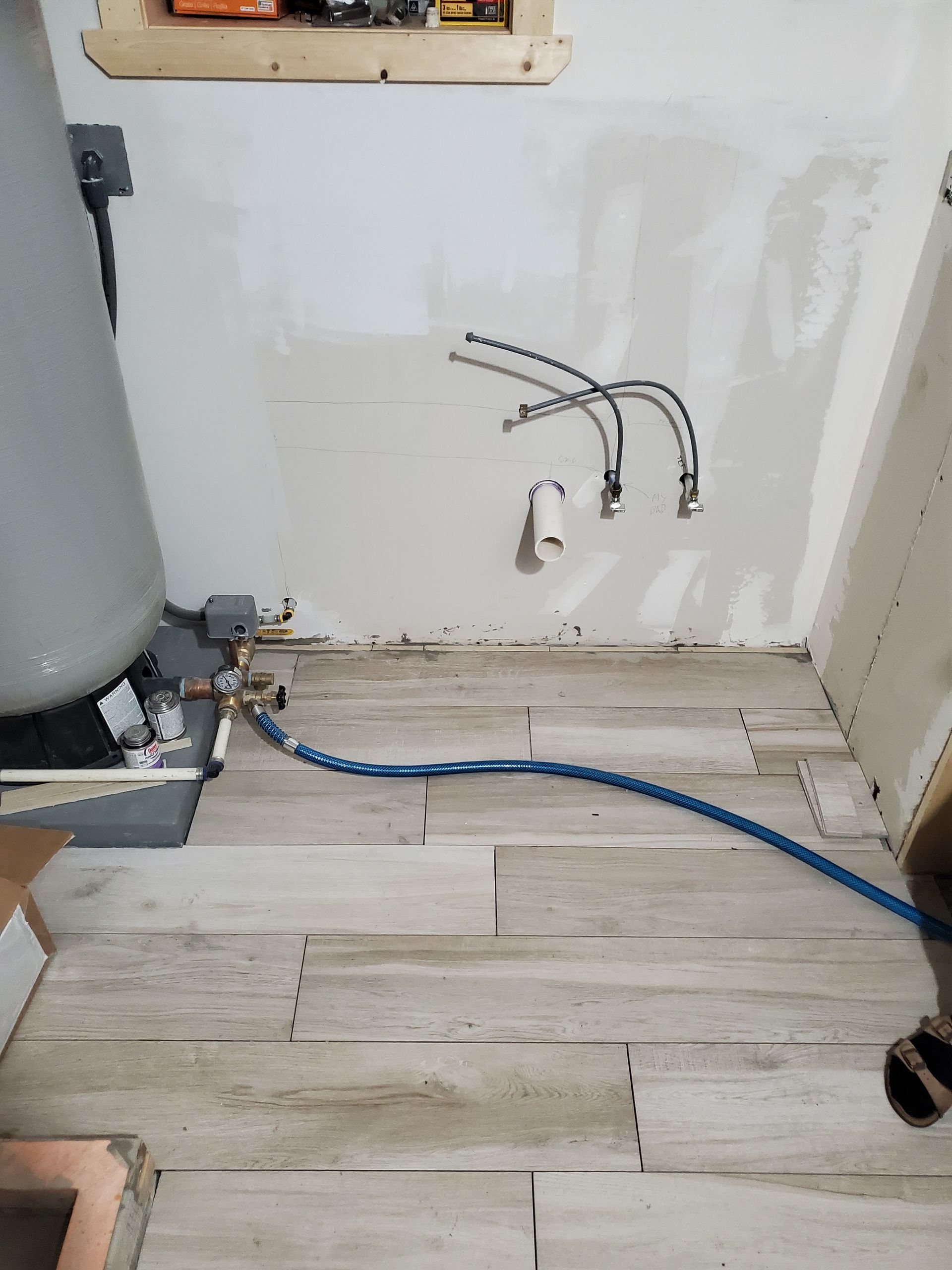 Bathroom under construction with new tile floor, water heater, exposed pipes and incomplete drywall.