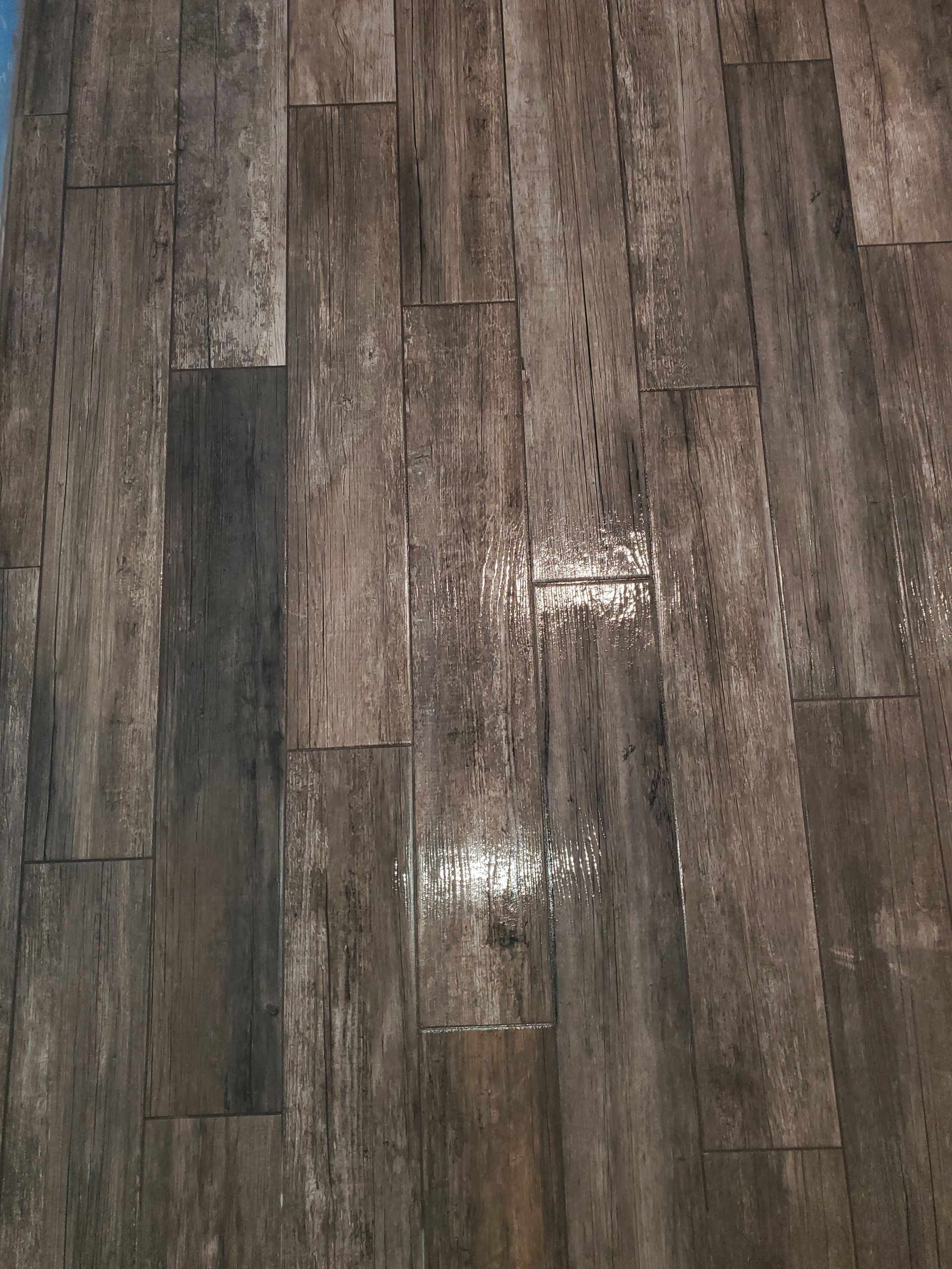 Hands in yellow gloves placing a beige tile, with tile spacers, on a mortar base.