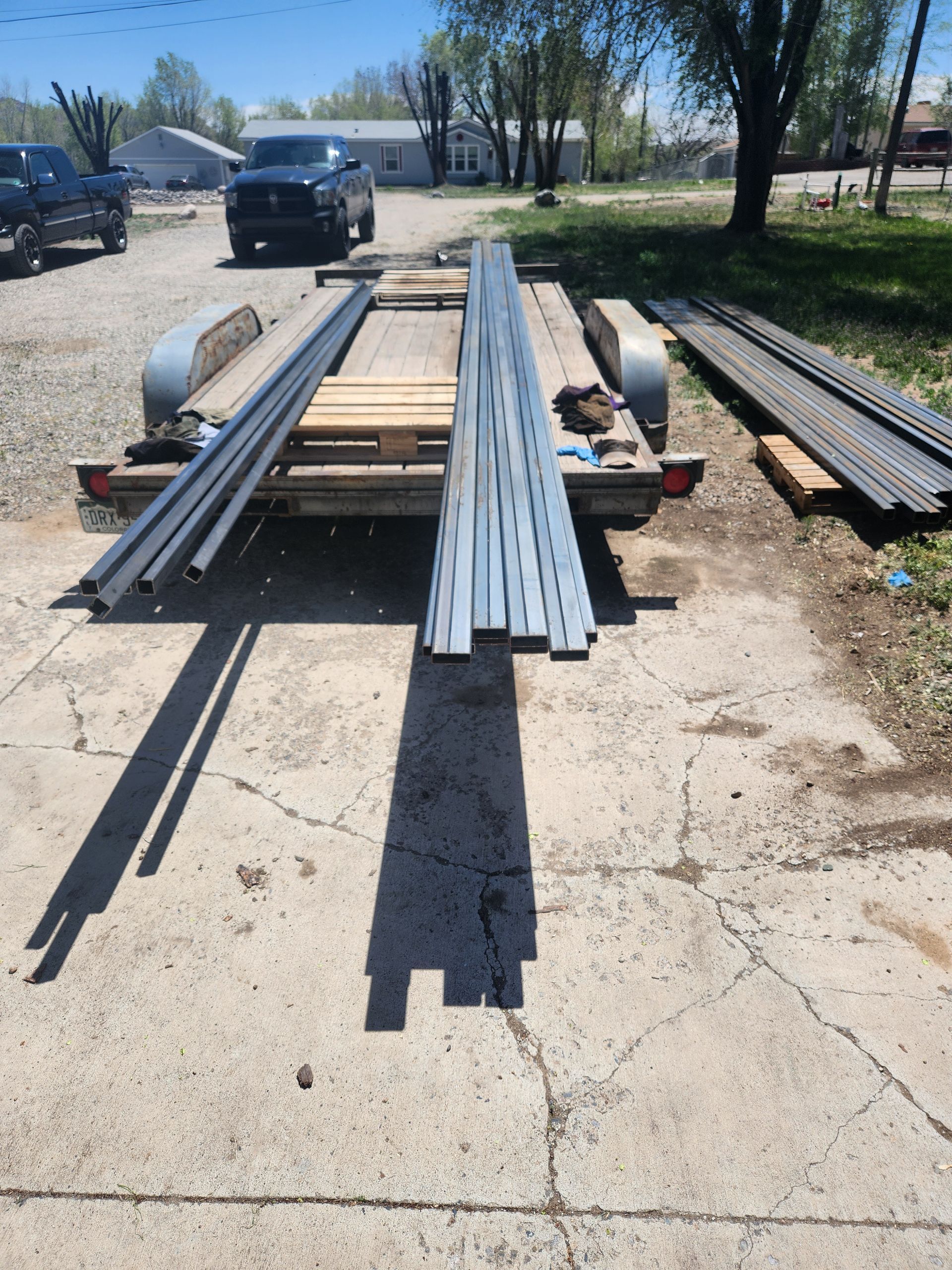 A trailer loaded with metal beams and pipes parked on concrete, outdoors.