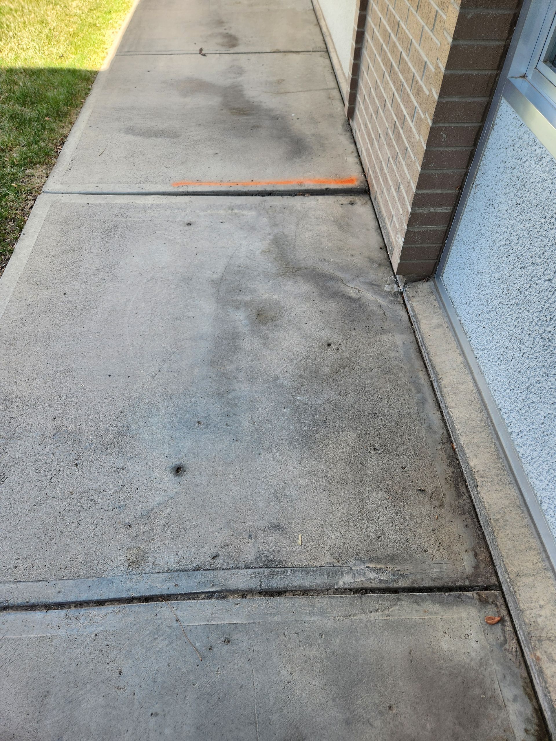 Concrete walkway beside a brick building with a window, grassy area to the left.