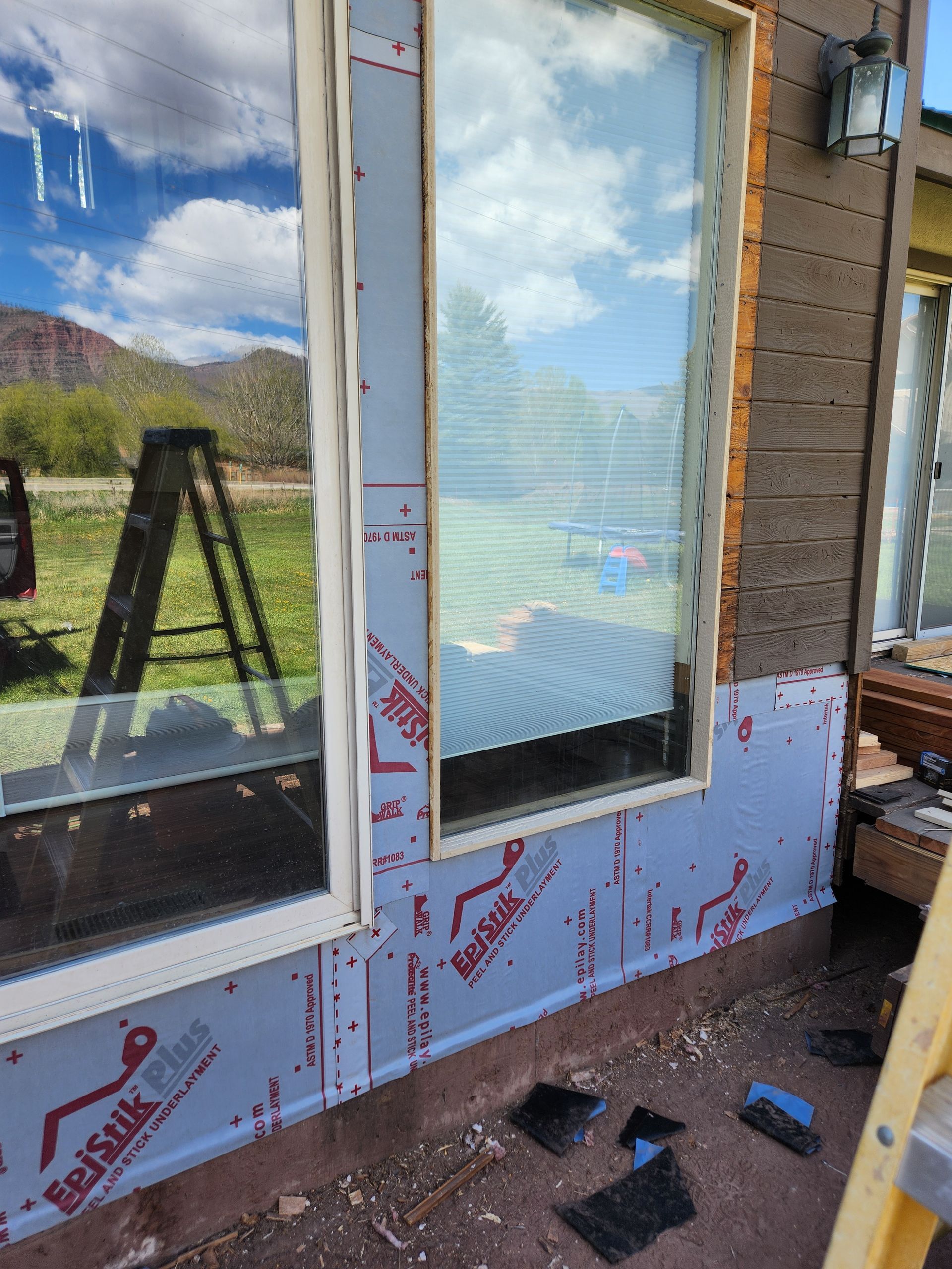 Exterior view of a house with windows; new construction. Blue protective wrap and ladder in the foreground.