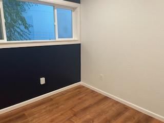Empty room with dark blue and white walls, wood-look floor, and a window.