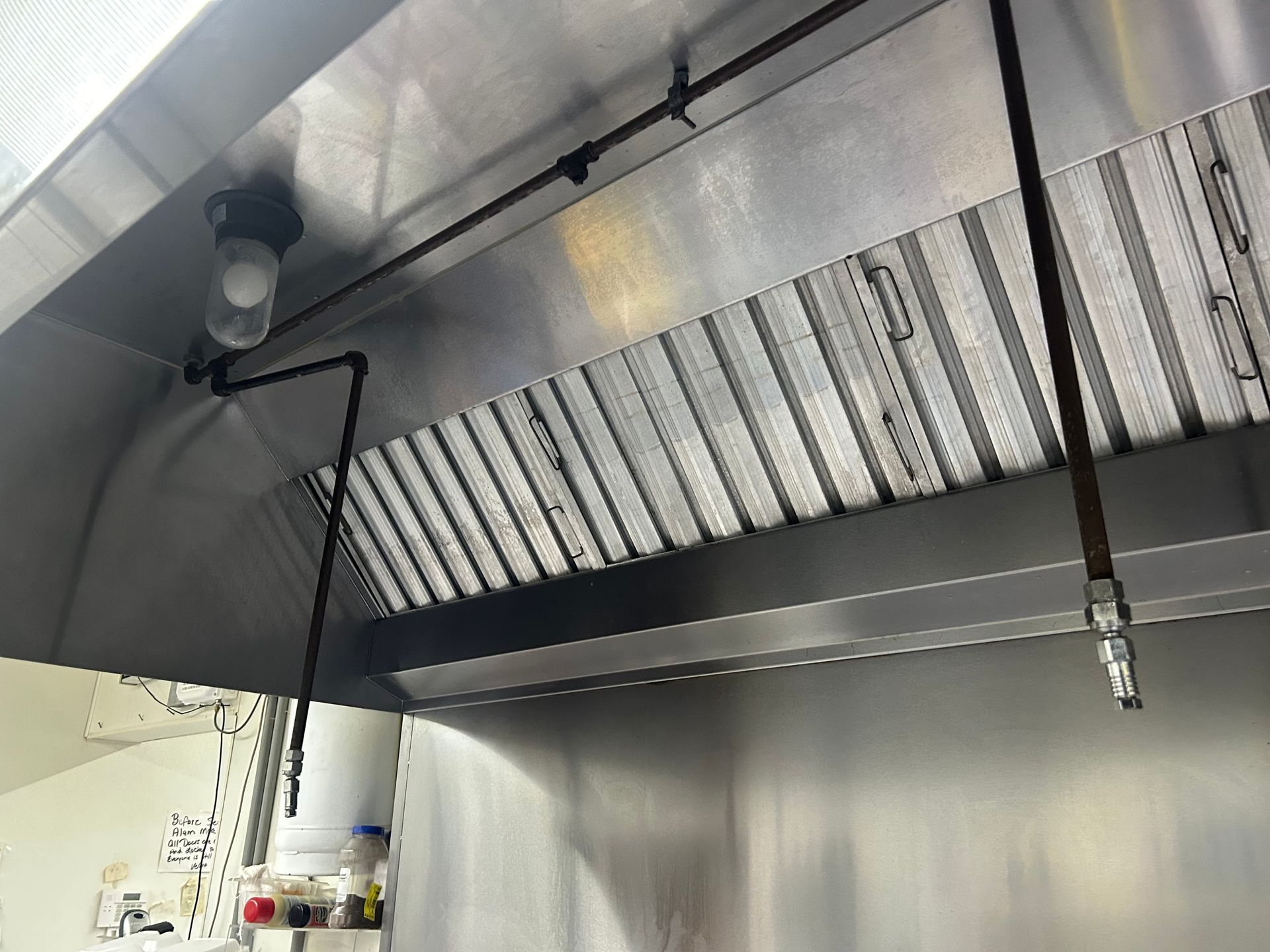 A stainless steel hood is hanging from the ceiling of a kitchen.