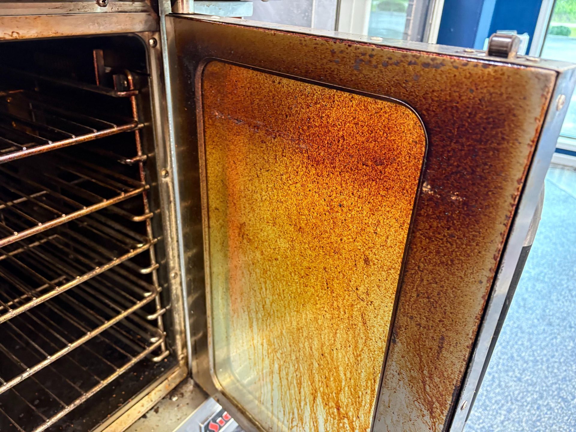 Open, dirty oven interior with stained glass door and wire racks.