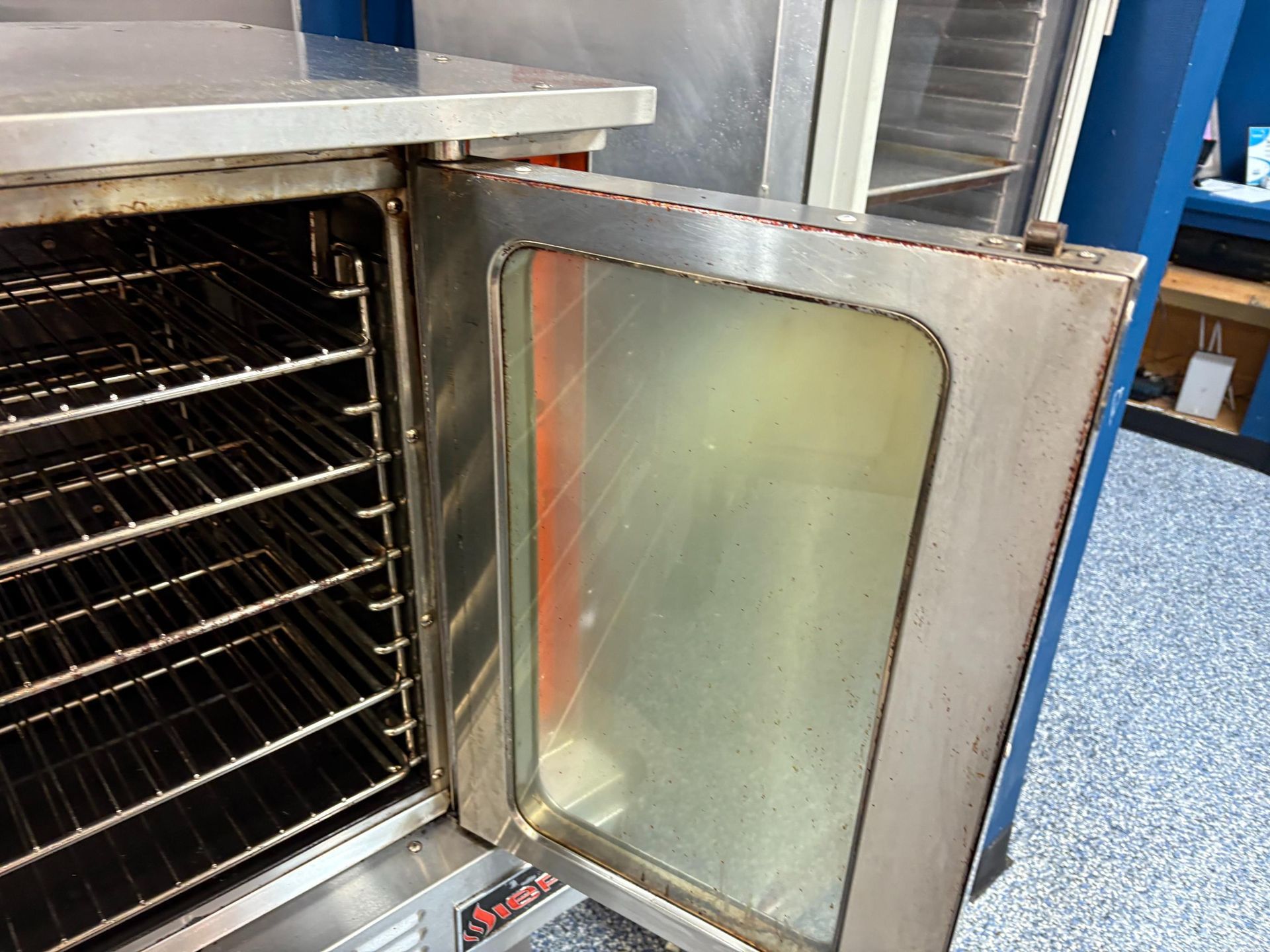 Commercial oven with open door, interior showing racks. Stainless steel, dirty glass.
