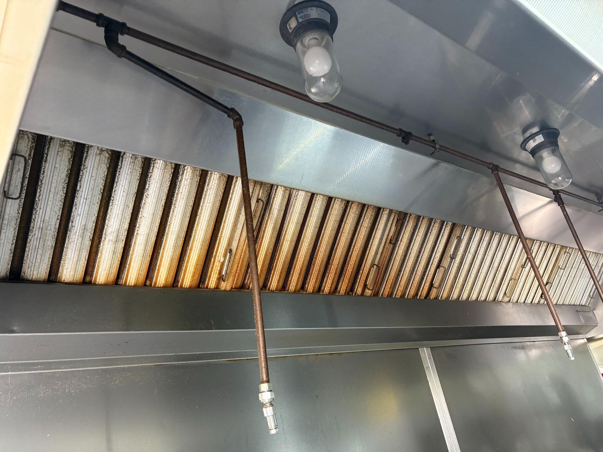 Greasy, stainless steel commercial kitchen exhaust hood with lights and fire suppression nozzles.