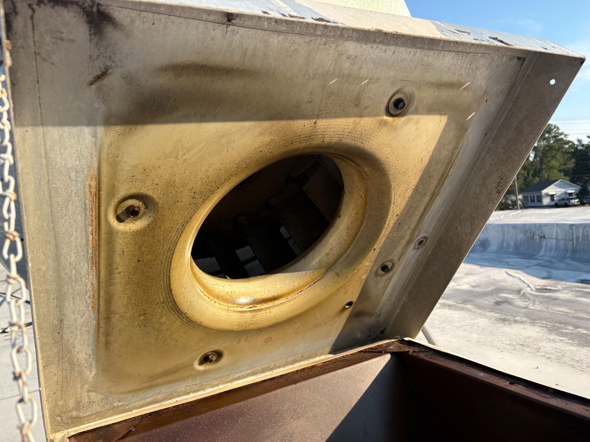 Square metal vent hood, open, revealing a dirty interior with a central oval opening.