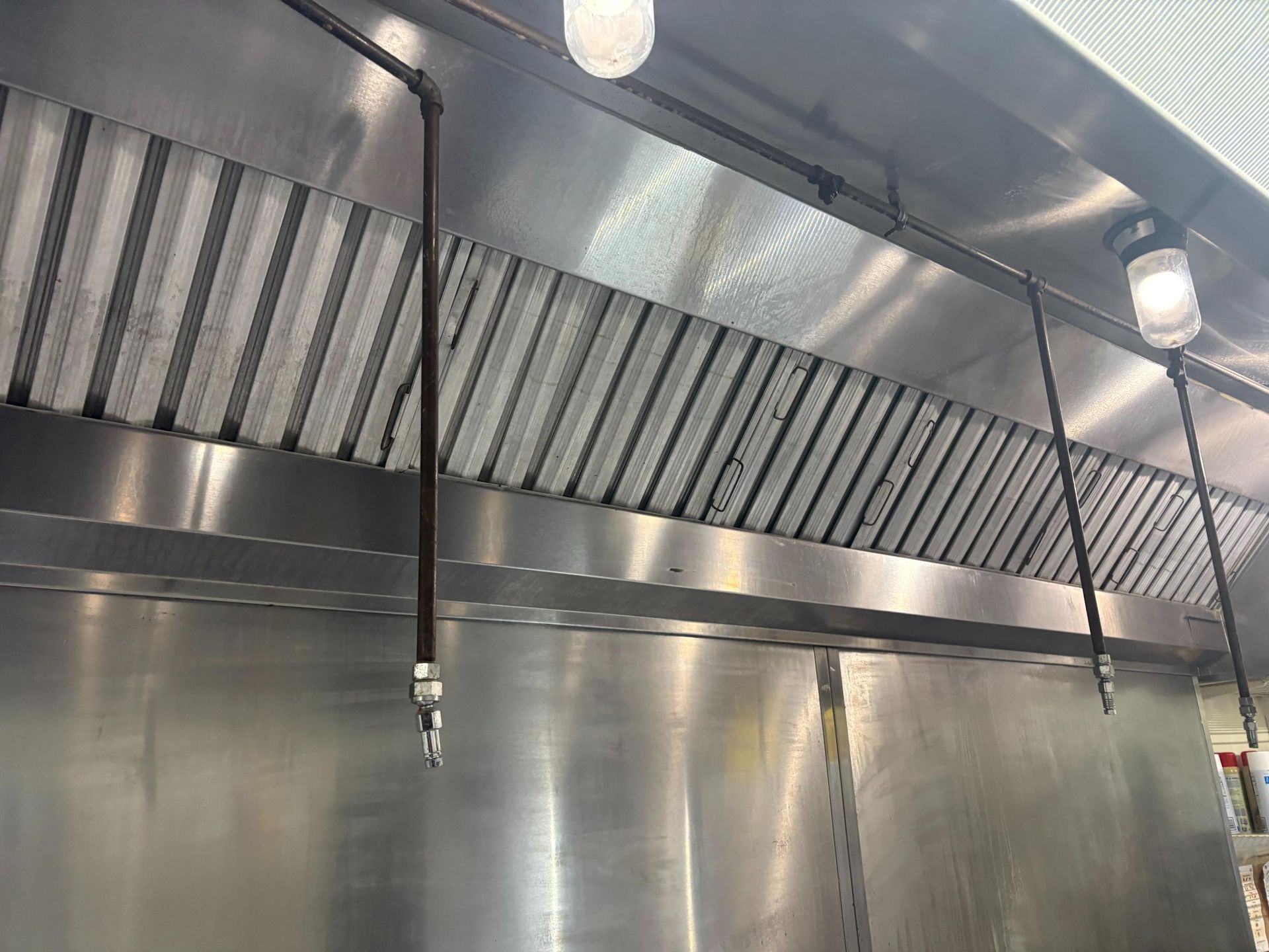 Stainless steel commercial kitchen exhaust hood with light and spray nozzles.