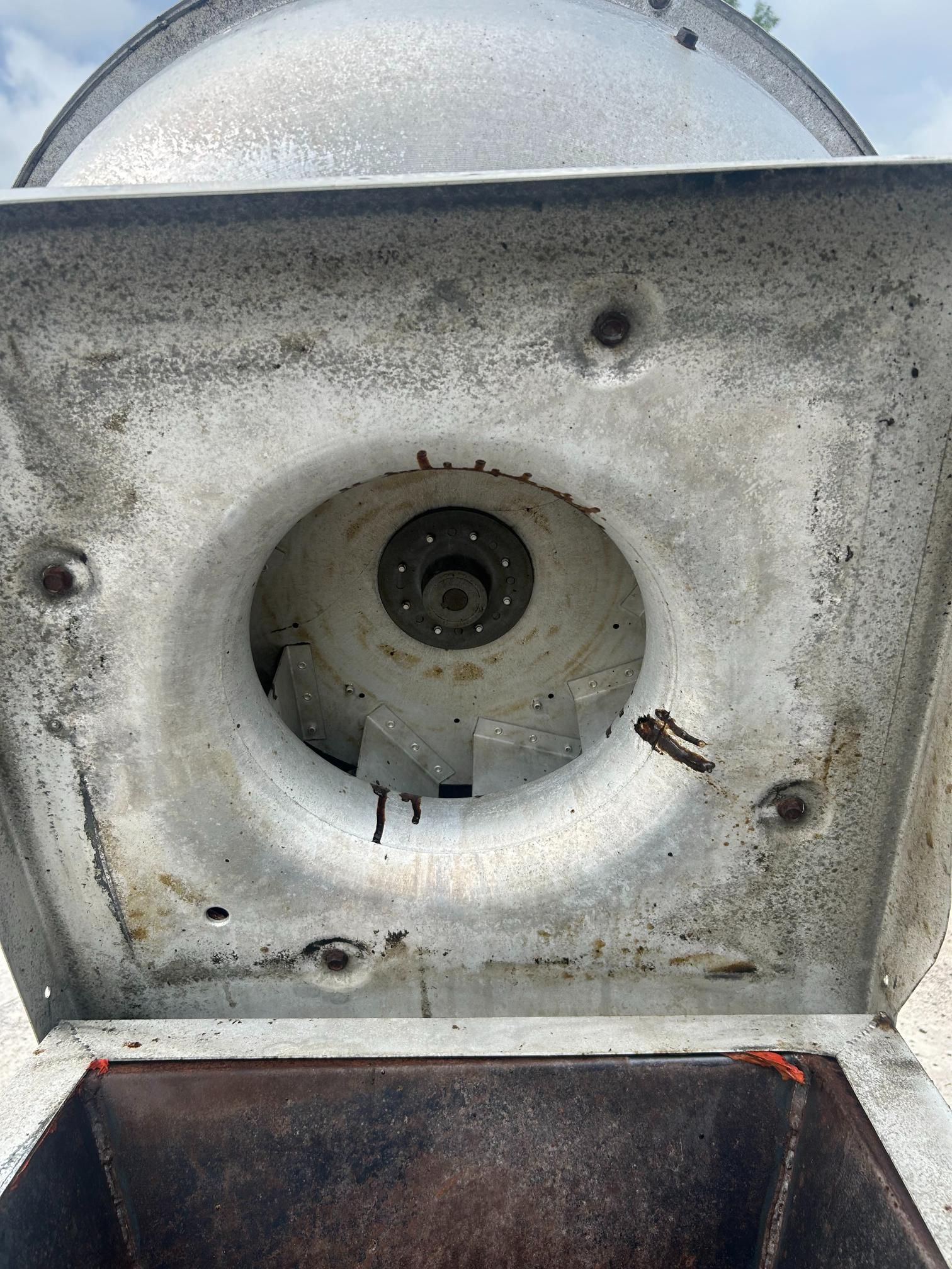 Inside of a weathered white metal machine.  A round center with a dark shaft surrounded by bolts.