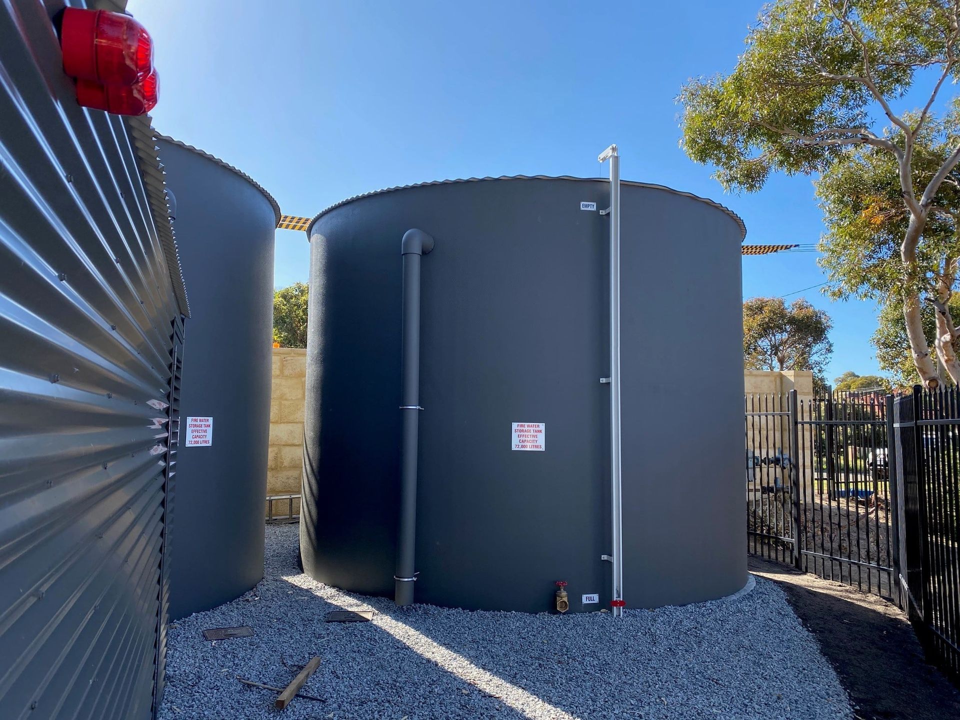 Two Large Gray Water Tanks Are Sitting Next To Each Other In A Gravel Area – Perth, WA - Armadale Concrete Tank Co.