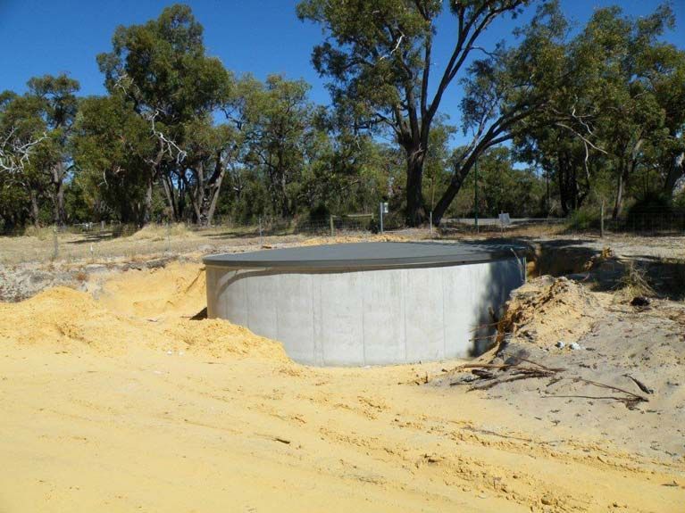 A Large Concrete Tank Is Sitting In The Middle Of A Dirt Field Surrounded By Trees – Perth, WA - Armadale Concrete Tank Co.