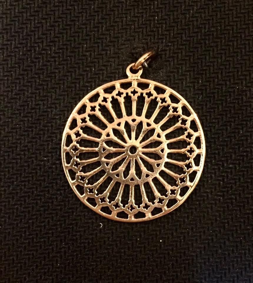 Ciondolo in oro a forma di rosa, dal design elaborato su uno sfondo scuro testurizzato.